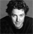 Black-and-white pixelated image of a person with curly hair wearing a dark jacket against a gradient background.