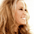 Pixelated close-up of a person with long light brown hair, smiling with visible teeth, wearing a dark top against a light background.