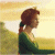 Pixelated profile of a person with brown hair tied in a ponytail, wearing a green top, standing against a yellowish background with blurred green and white areas.