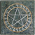 A circular icon with a golden-brown border and intersecting white lines forming a star-like pattern on a dark gray pixelated background.