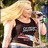Pixelated image of a person with long blonde hair wearing a dark sleeveless top, holding a small object near their face.