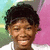 Pixelated portrait of a person with short dark hair, closed eyes, and a smiling mouth, wearing a white shirt against a background with green, blue, and pink sections.
