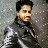 Pixelated static image of a person with dark hair wearing a high-collared jacket against a speckled gray background.