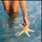 A pixelated image shows a person in a light-colored swimsuit holding a starfish against a blue water background.