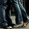 Two people standing close together, wearing blue jeans and shoes with colorful patterns on the soles.