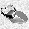 A grayscale heart-shaped icon with a glossy surface and a dark curved line inside, casting a soft shadow on a textured background.