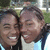 Two people in light blue and white shirts smile closely together against a blurred green background.