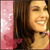 A pixelated image shows a person with long brown hair smiling, wearing a red top against a pink background with white sparkles.