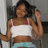 A pixelated static image shows a person with dark hair wearing a white crop top with red straps and light blue bottoms, raising one hand near their head.