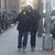 Two figures in dark coats walk side-by-side on a snowy path with blurred background structures.