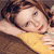 A pixelated close-up of a person with brown hair wearing a yellow top, lying down with one arm behind their head.