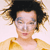 Pixelated close-up of a person with dark curly hair, light skin, and a yellow garment against a light background.