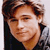 Pixelated close-up of a person with light brown hair wearing a dark top against a light background.
