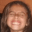 Pixelated close-up of a person with long dark hair, closed eyes, and an open mouth showing teeth against a brown background.