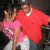 Two people in red and pink shirts pose together, one making a hand gesture while the other adjusts their hair.