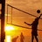 Silhouette of a person playing volleyball at sunset with net and ball, set against warm orange sky.