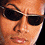 Pixelated close-up of a person's face wearing dark sunglasses with light frames, showing partial facial features and warm-toned skin tones.