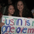 Two people stand behind a sign with multicolored text reading "Turn Me On" in a pixelated image.