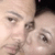 Two people in close proximity with one person's face partially visible, showing eyes and nose, against a dark background.