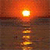 A static pixelated image of a bright sun setting over water, with warm orange and red tones dominating the sky and reflecting on the water's surface.
