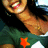 A person with long dark hair wears a green shirt over white, smiling broadly with visible teeth and red lips.
