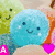 four identical blue circular characters with smiling faces, each holding a pink heart, against a background of green smiling characters