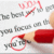 A hand holding a red pen draws pink circles around gray text on a white background.