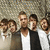 Group of men in white and dark clothing standing against a textured background with 'OneRepublic' text above.