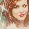 A static pixelated image of a person with shoulder-length brown hair, green eyes, and red lipstick, smiling with visible teeth against a blurred background.