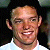 Static pixelated image of a person's face with a light-colored shirt, dark hair, and a neutral expression against a dark background.