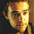 Pixelated close-up of a person's face with light brown hair, dark eyebrows, and a neutral expression against a dark background.