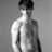 Black-and-white photo of a shirtless person with short hair against a gray background, surrounded by green pixelated text on a black field.