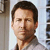 A pixelated close-up of a person with short dark hair wearing a light-colored shirt against a blurred background with vertical elements.