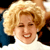 Static pixelated image of a person with blonde hair wearing a white top and dark outer garment, cropped to show only the upper body against a black background.