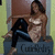 Pixelated image of a person in dark pants and light top sitting on a blue surface with 'CuteBaby' text, against brown and green background.