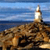 A static pixelated image shows a lighthouse on a rocky coastline with blue sky and water in the background.