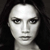 Pixelated grayscale portrait of a person with dark hair against a dark background, showing facial features and neck in a static close-up.
