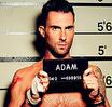 Static image of a shirtless man holding a mugshot-style sign in front of a height chart background, with visible pixelation and dithering effects.