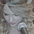 A woman with light brown curly hair holds a silver microphone, her expression shifts from neutral to smiling across frames.