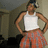 Pixelated image of a person wearing white tank top and orange patterned pants, standing with hands on hips against blurred background.