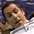 Pixelated close-up of a person's face with light skin tone, brown hair, and a white shirt against a dark blue background.