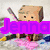 Pixelated cartoon character with brown blocky head and limbs holding a baseball bat, standing on pink flowers in grassy background.