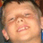 Pixelated close-up of a person's face showing a grimacing expression with squinted eyes and bared teeth, set against a blurred background.