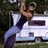 A person in dark top and light pants holds another person above their head against a white vehicle background.