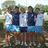 Six pixelated figures in blue and white athletic wear stand closely together outdoors with greenery behind them.