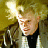 Pixelated static image of a person with light hair wearing dark clothing against a yellowish background, featuring bright lighting effects on the left side.
