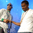 Two pixelated figures in white shirts stand against a blue background, one with a green collar detail, arms crossed, the other with a light blue collar detail, both facing left.