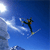 Pixelated static image of a skier in mid-air against a blue sky background with white cloud-like streaks and bright light source on left.