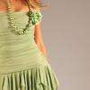 A cropped image shows a person wearing a light green dress with a textured bodice and vertical pleats on the skirt, against a plain light gray background.