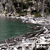 Pixelated static image showing a blurred natural scene with water, rocks, and foliage in muted greens, grays, and browns.